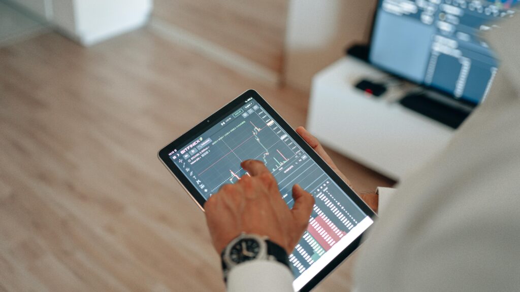 A person holding a tablet indoors displaying financial trading graphs, engaging in digital finance analysis.