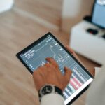 A person holding a tablet indoors displaying financial trading graphs, engaging in digital finance analysis.
