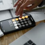 Close-up of a person using a smartphone calculator on a table with documents for financial calculations.