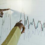 Hands pointing at a financial stock chart on a digital screen, highlighting data analysis and trends.
