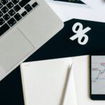 Overhead view of a workspace with a laptop, smartphone displaying a chart, and notebook for financial analysis.