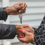 Close-up of a realtor handing over a house key to a new homeowner, symbolizing ownership and investment.