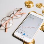 Smartphone displaying cryptocurrency graph alongside bitcoin coins and eyeglasses.