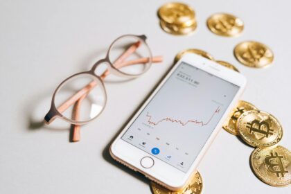 Smartphone displaying cryptocurrency graph alongside bitcoin coins and eyeglasses.
